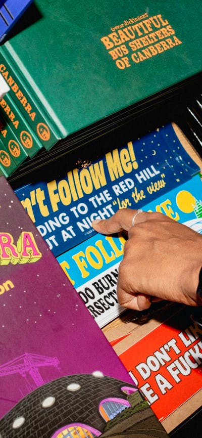 A close-up of a shopper’s hand browsing a selection of Canberra-themed books, stickers