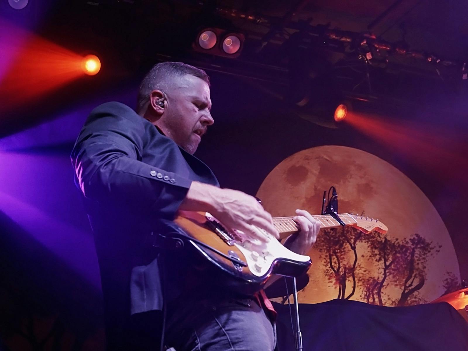 Mitchell Jon playing a Fender Strat guitar with moon backdrop and stage lights