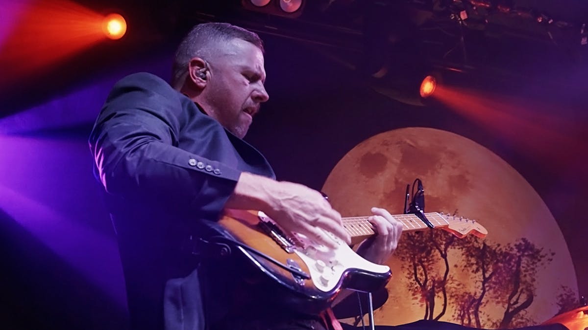 Mitchell Jon playing a Fender Strat guitar with moon backdrop and stage lights