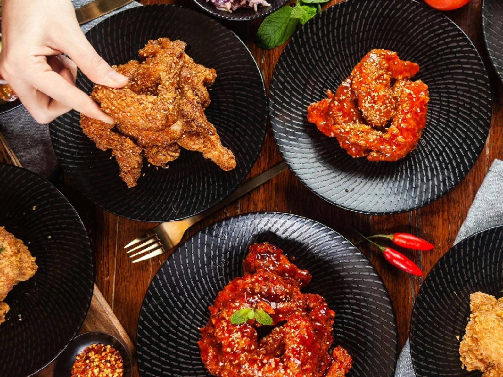 한국식 프라이드치킨 한 조각과 다른 프라이드치킨 조각 접시를 들고 있는 손