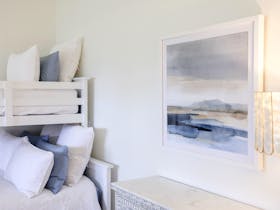 Bunk bed with white bedding beside a chest of drawers and framed artwork.