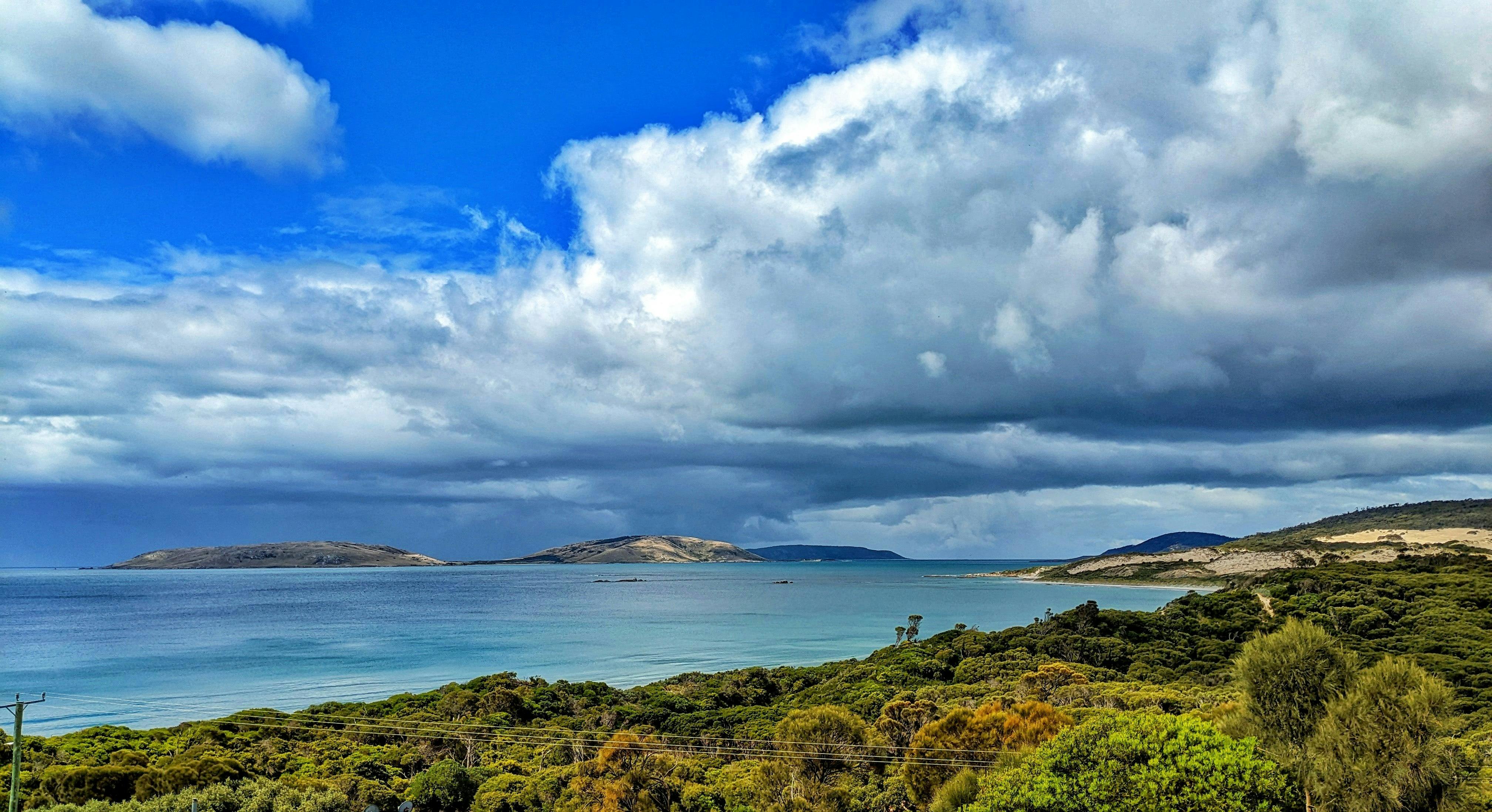 View of the Sister Islands and Blyth Bay with dramtic clouds above. Green trees in foreground