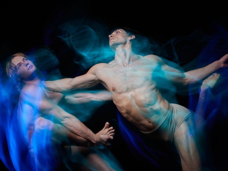 Two dancers bathed in blue light stand together.