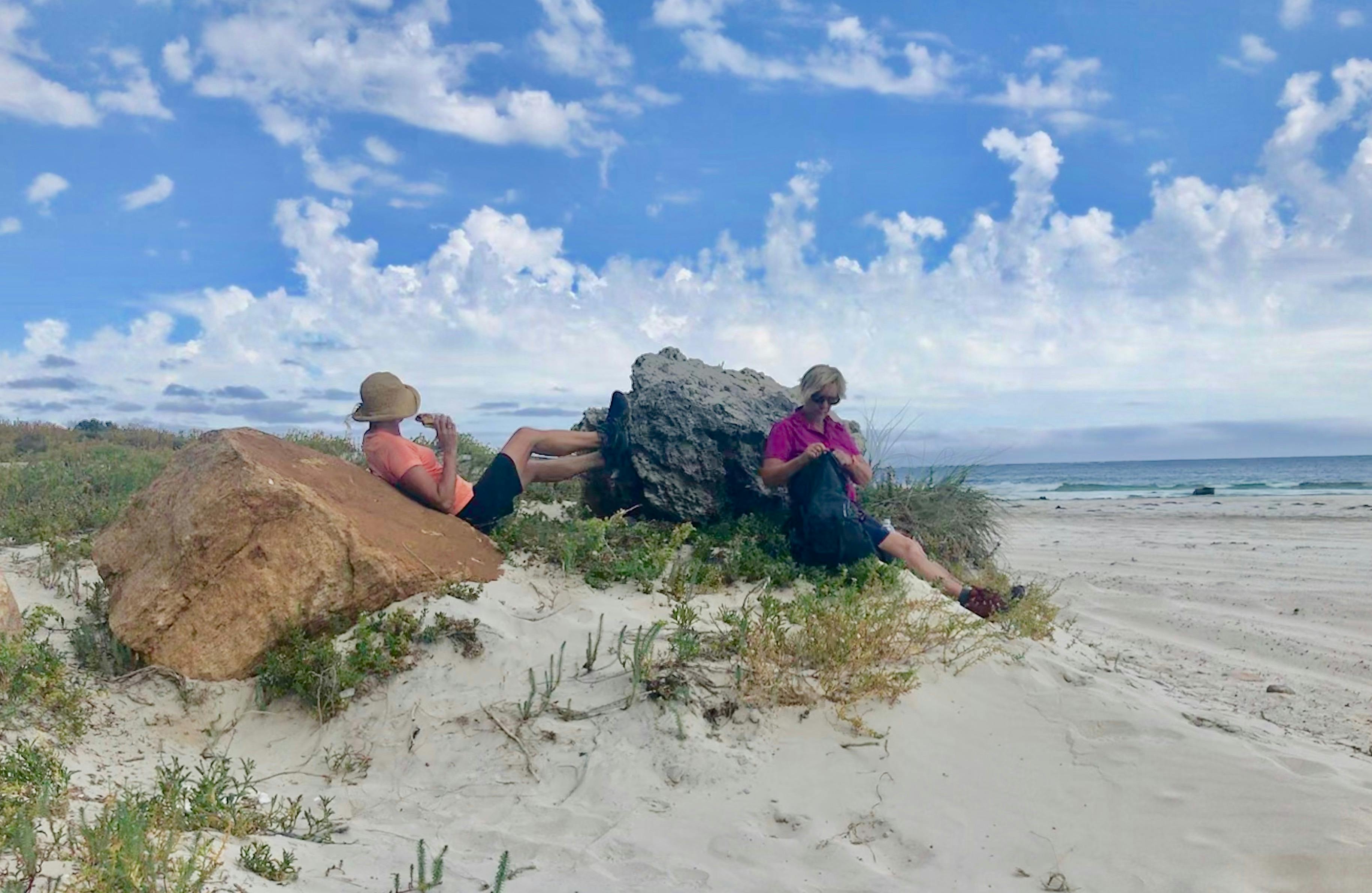 Two female hikers relax on the beach eating lunch