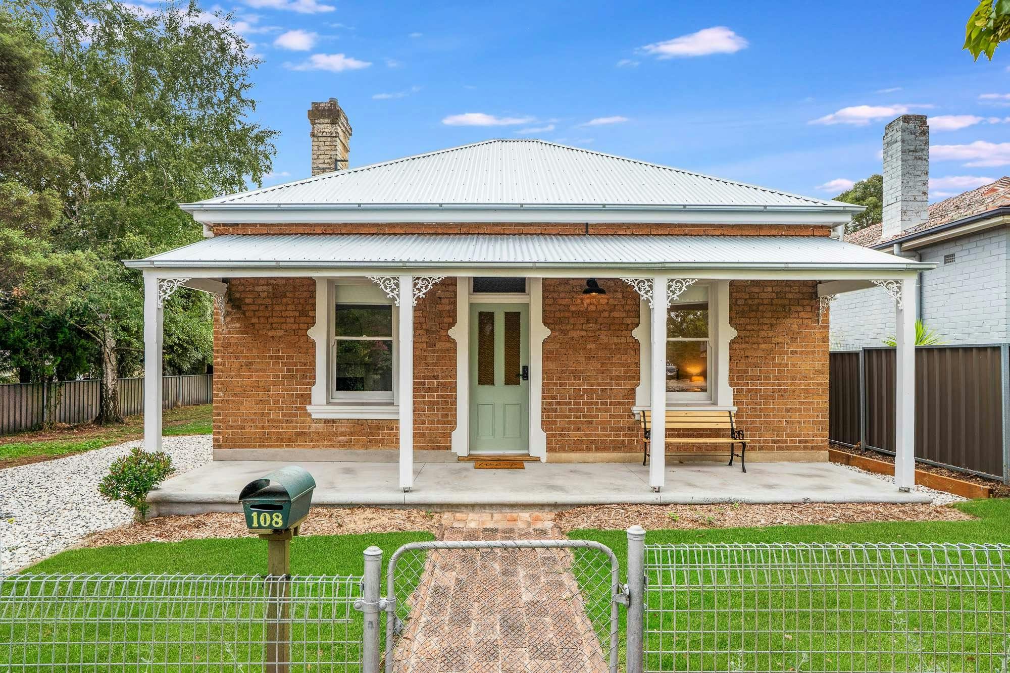 Old heritage brick home with gorgeous front awning and verandah. Green grass and a brick path
