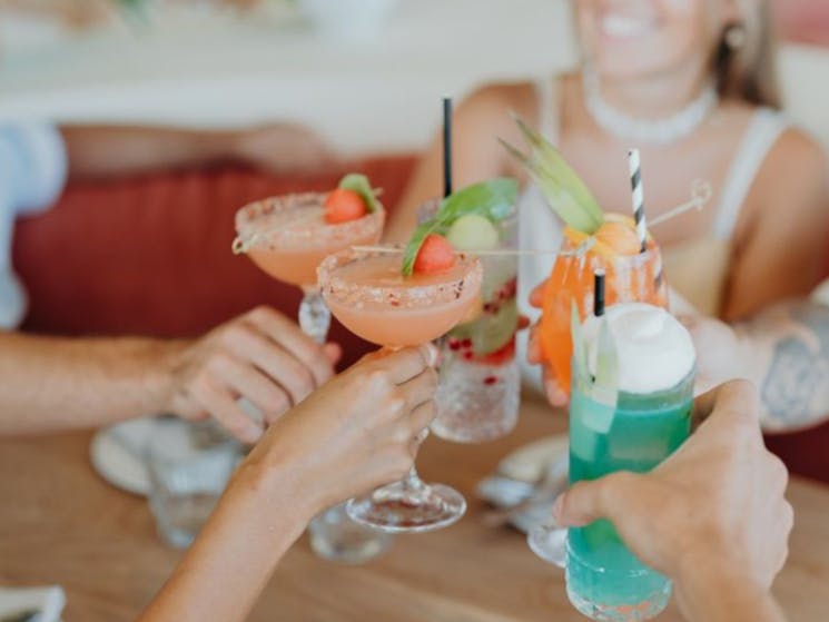a group of friends with bright coloured cocktails doing a cheers
