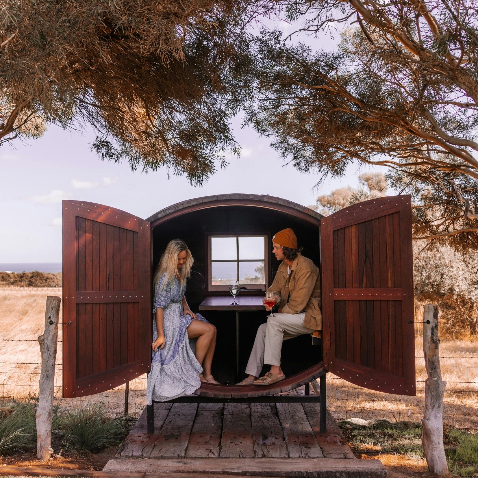 a couple sitting in the wine barrel tasting pod