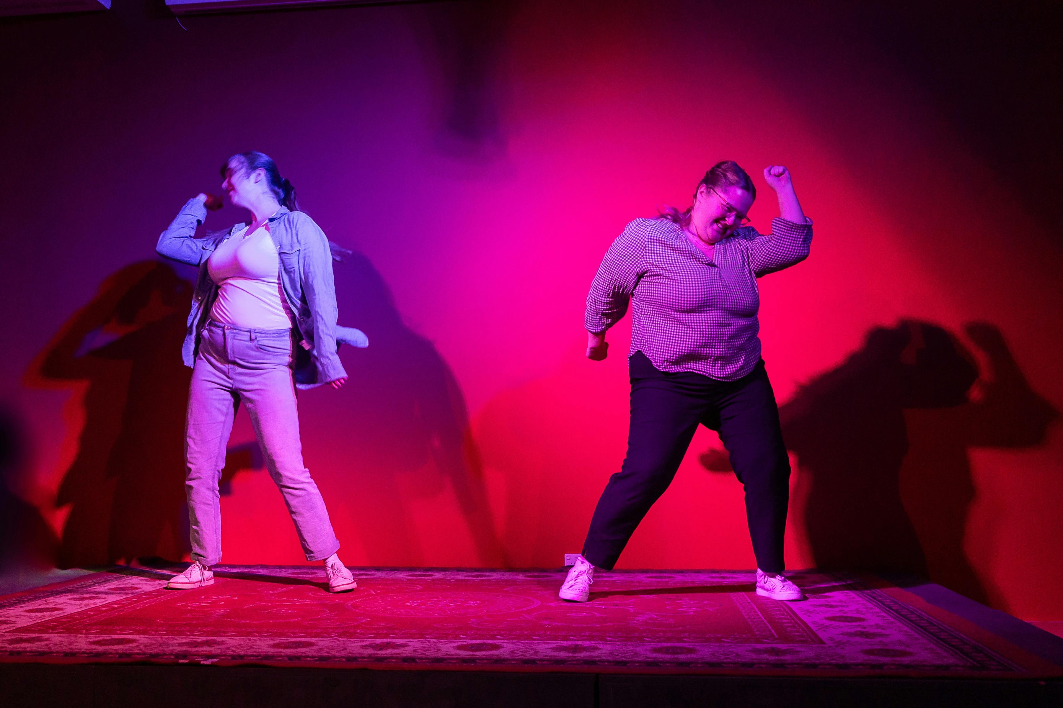 Two young women dance on a vividly lit stage.