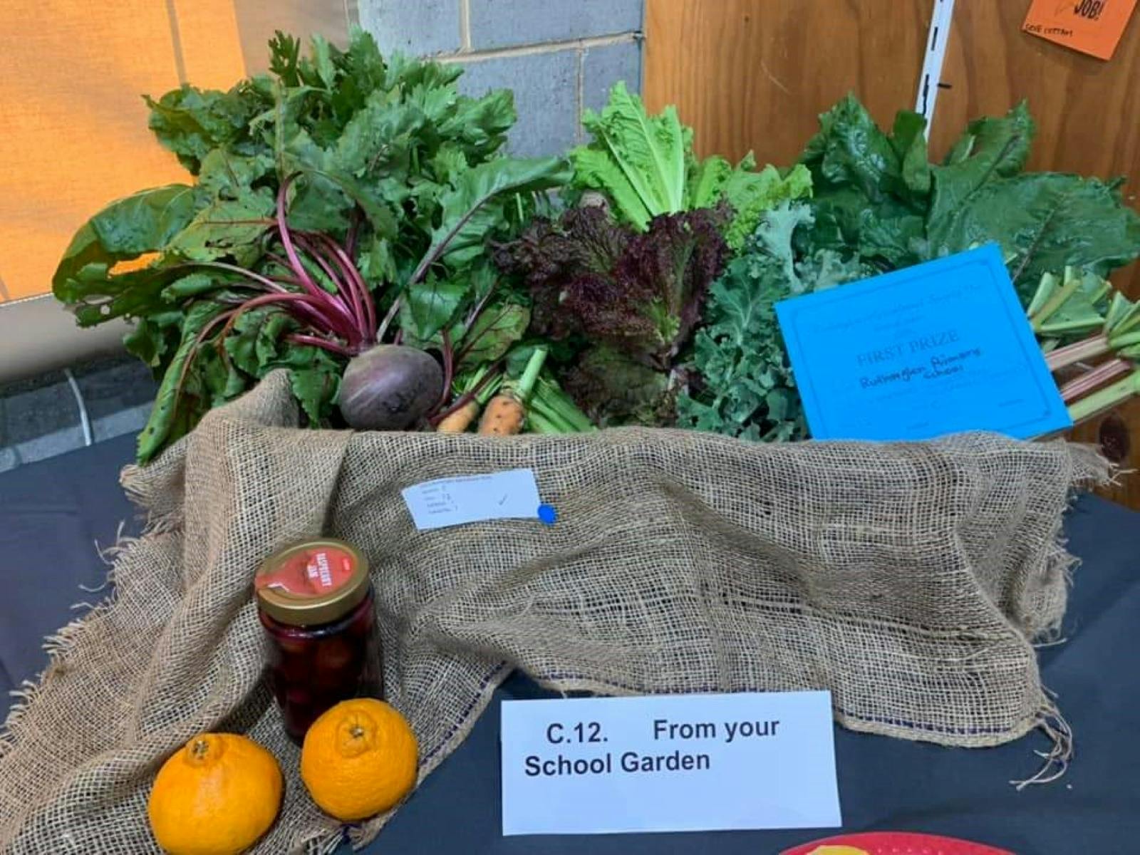 Photo of various school grown garden produce displayed in a basket, with first prize card.