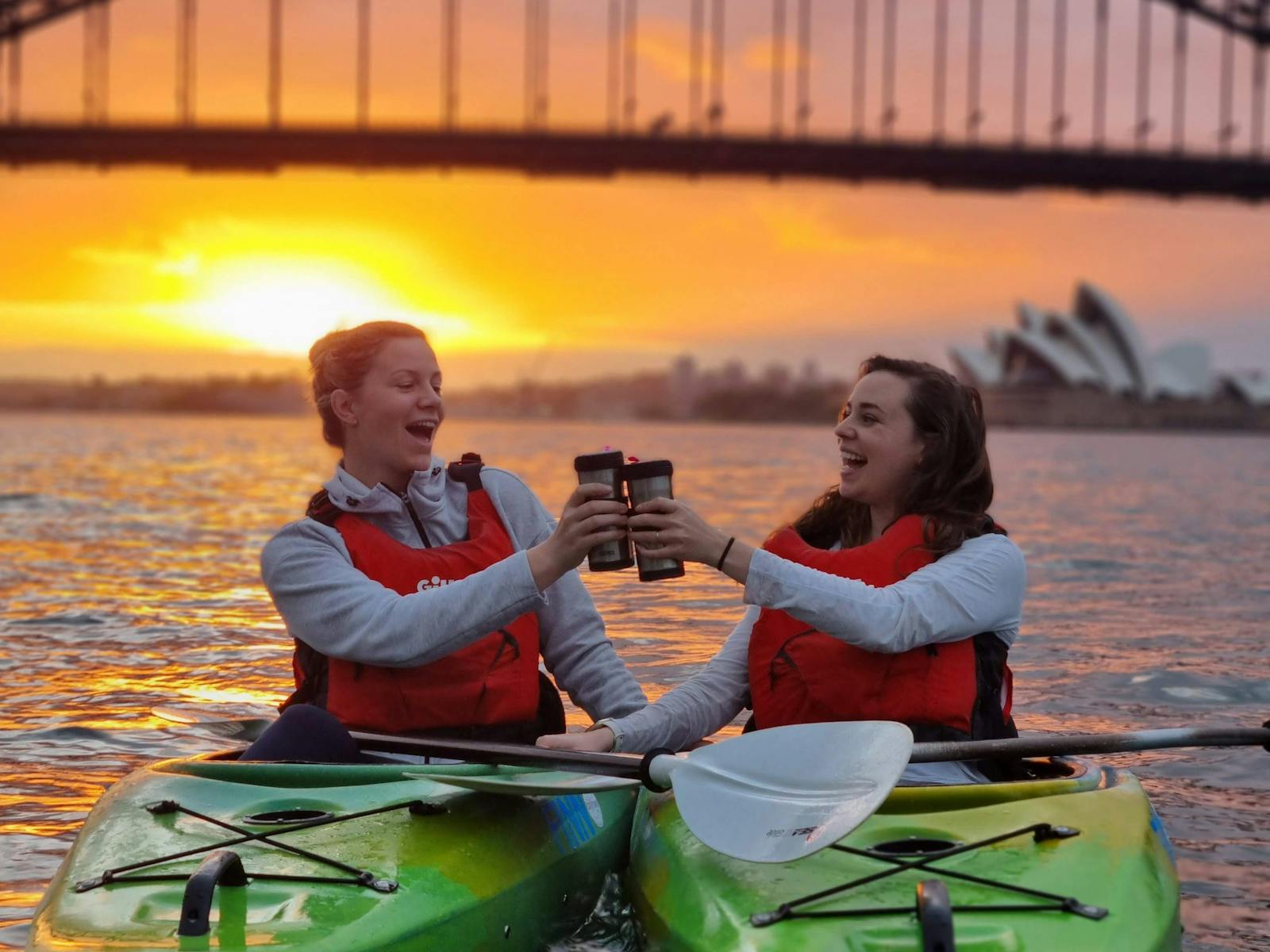 Two Kayakers cheersing coffees with a beautiful sunrise in the background on Sydney Harbour