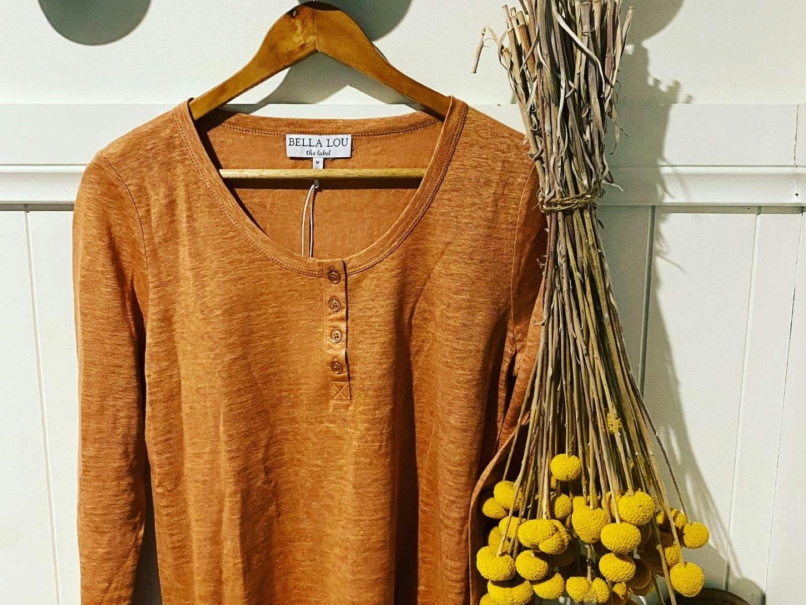 Bella Lou brown long sleeved shirt hanging next to dried yellow flowers