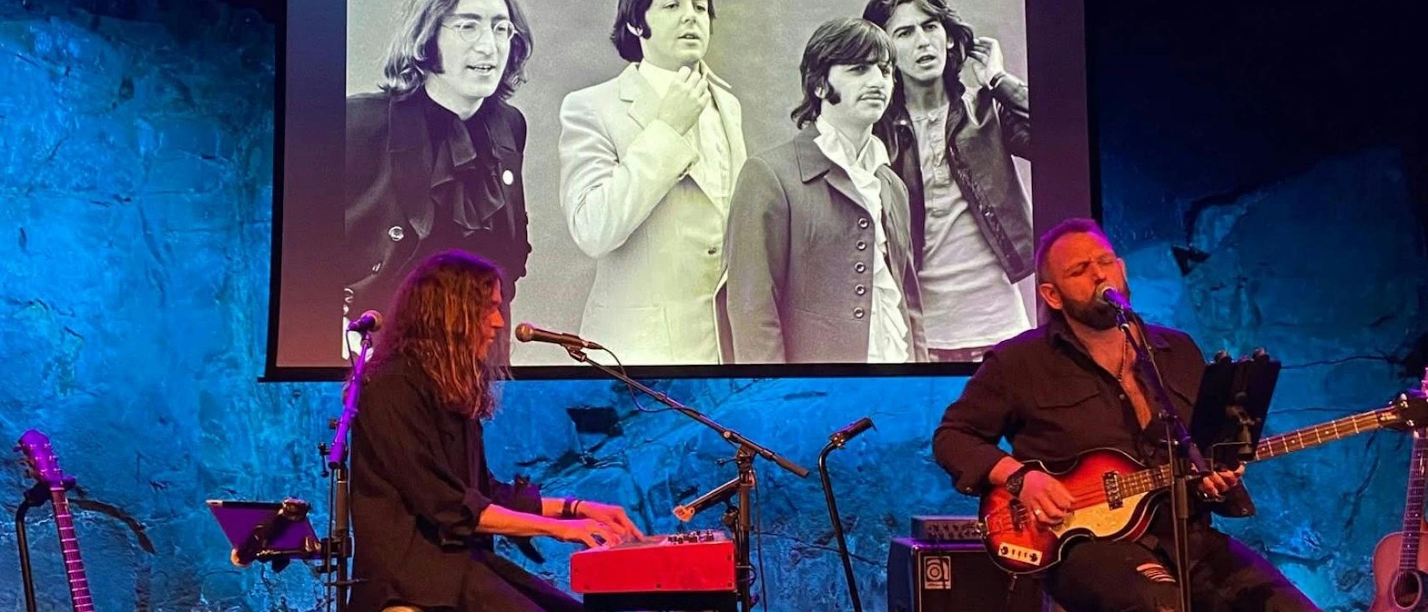 Two musicians sitting on stage, singing and playing instruments.