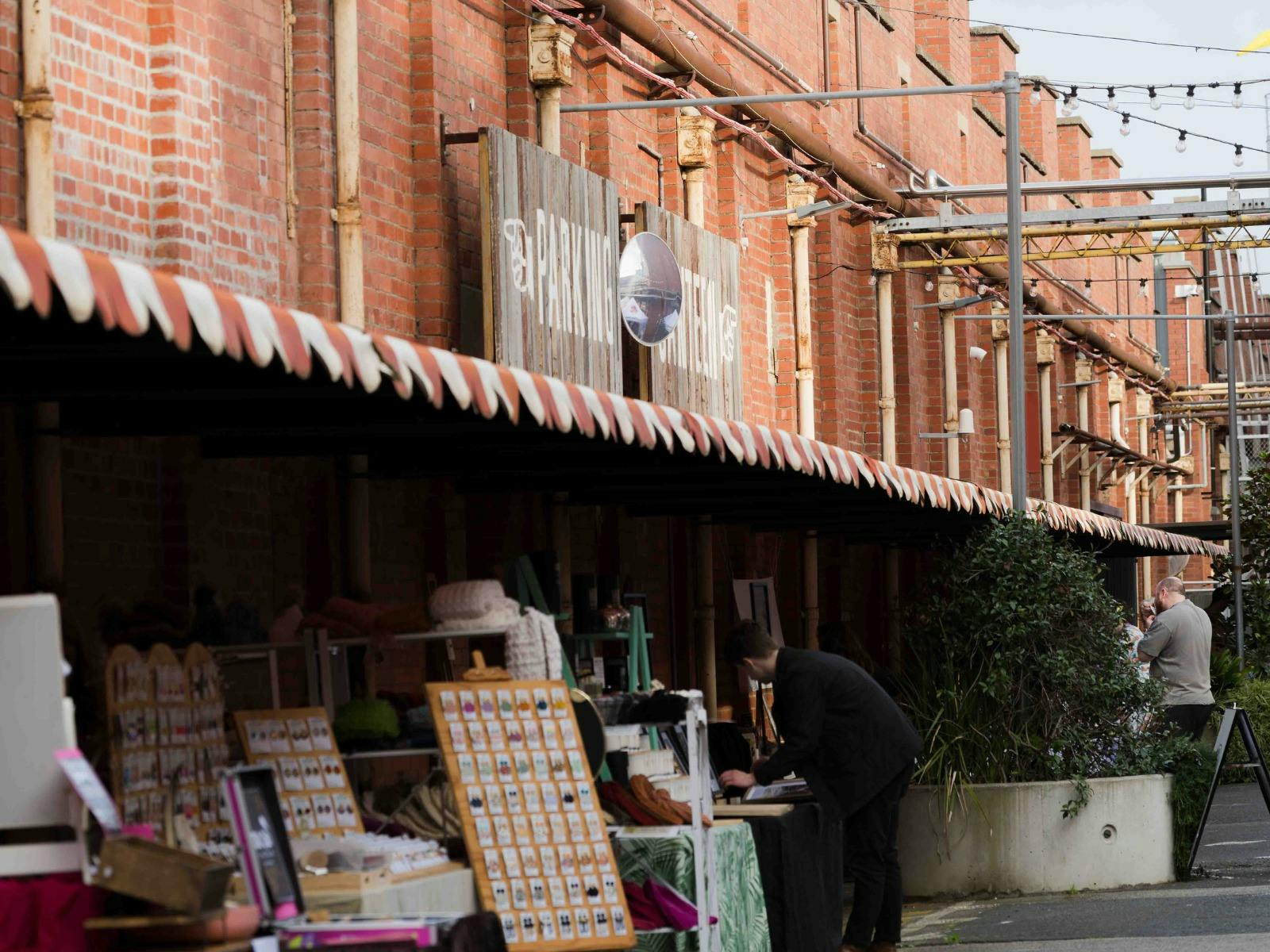 Outdoor market stalls beneath striped awnings in a red-brick brewery laneway.