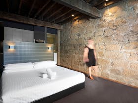 Blurred woman walks past king-sized bed and sandstone walls