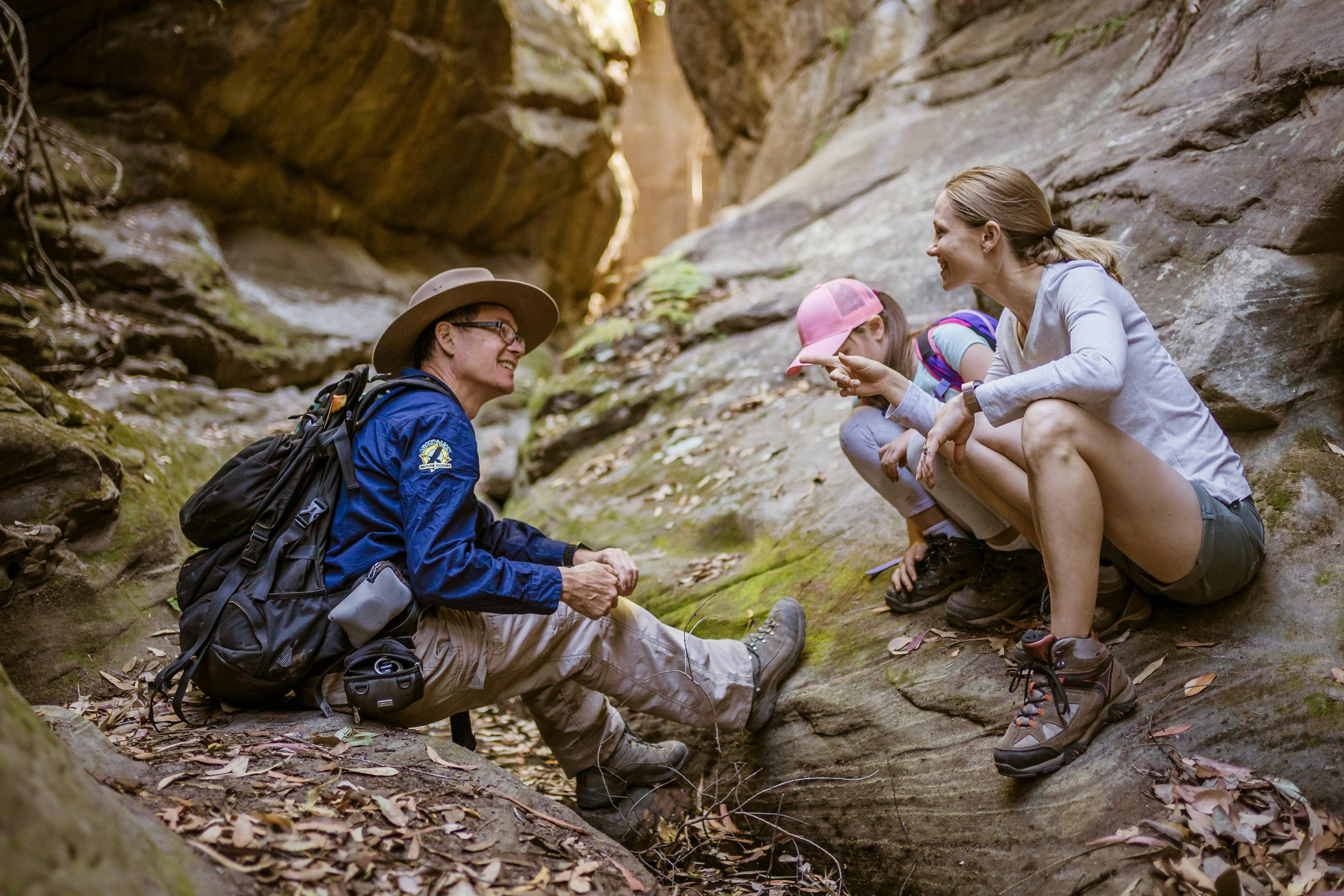 Tour guide and guests sit together inspecting something on the floor of a dry creek, Carnarvon Gorge