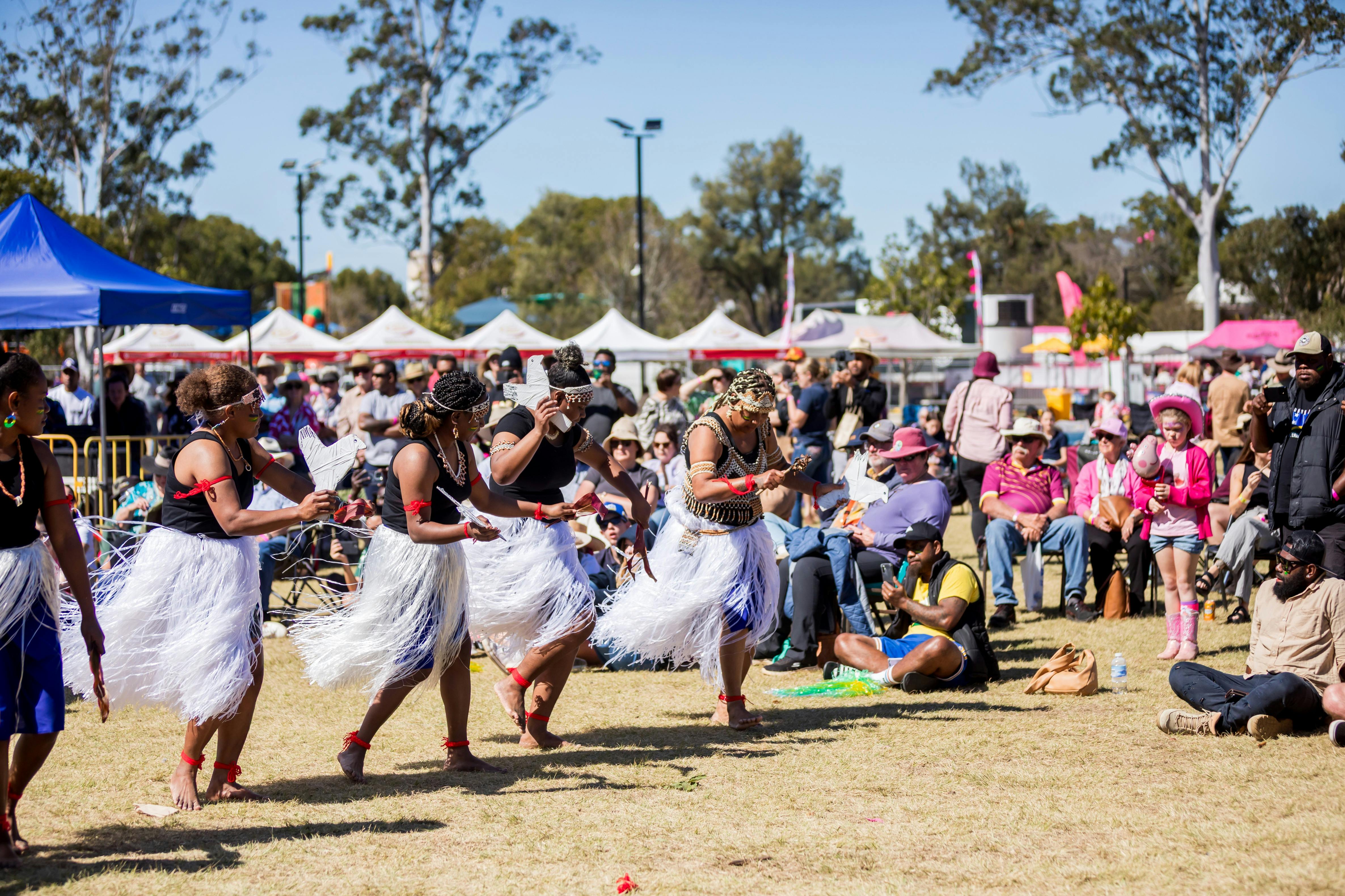 Women wearing white raffia skirts are performing a dance.