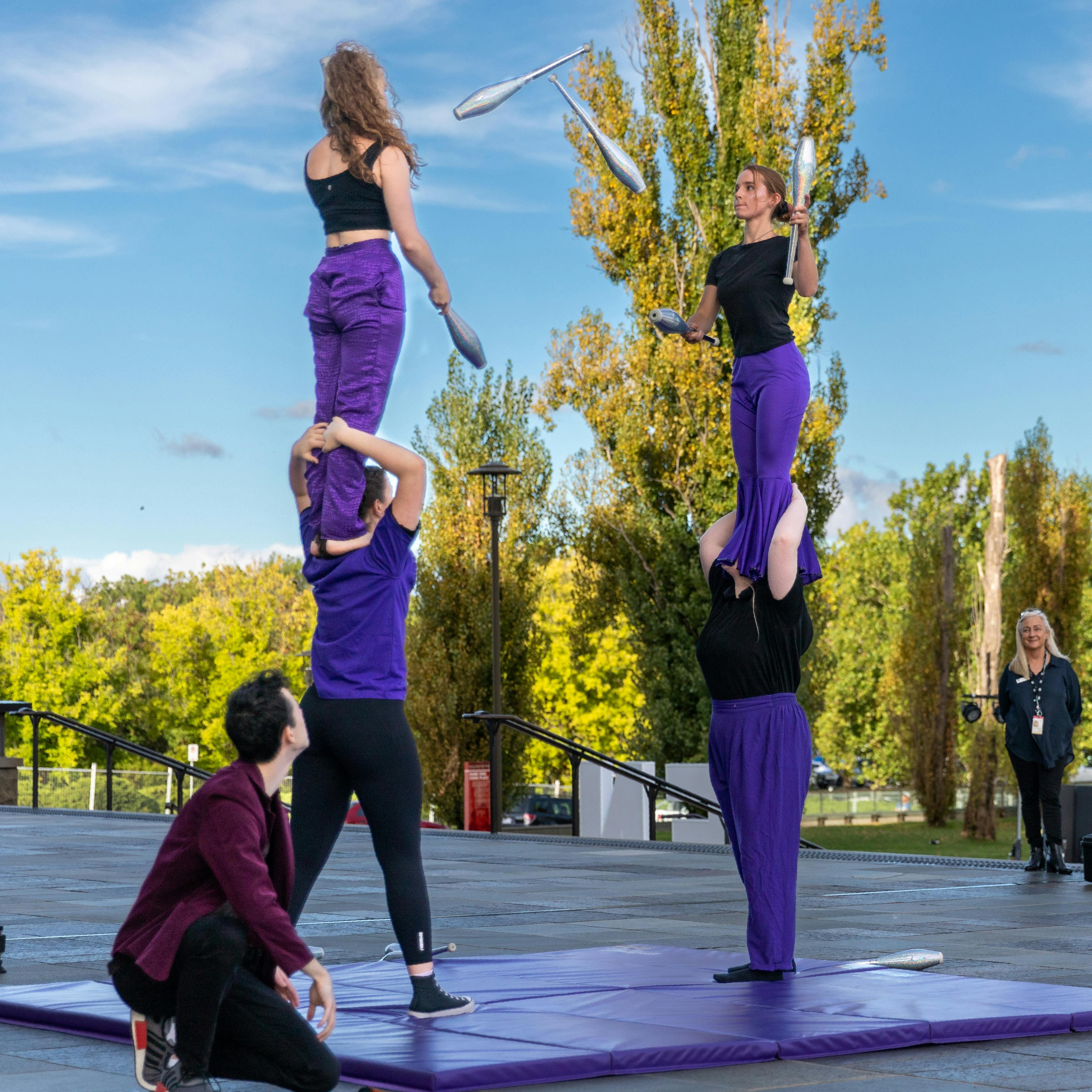 Warehouse Circus artists juggle to each other while balanced on shoulders