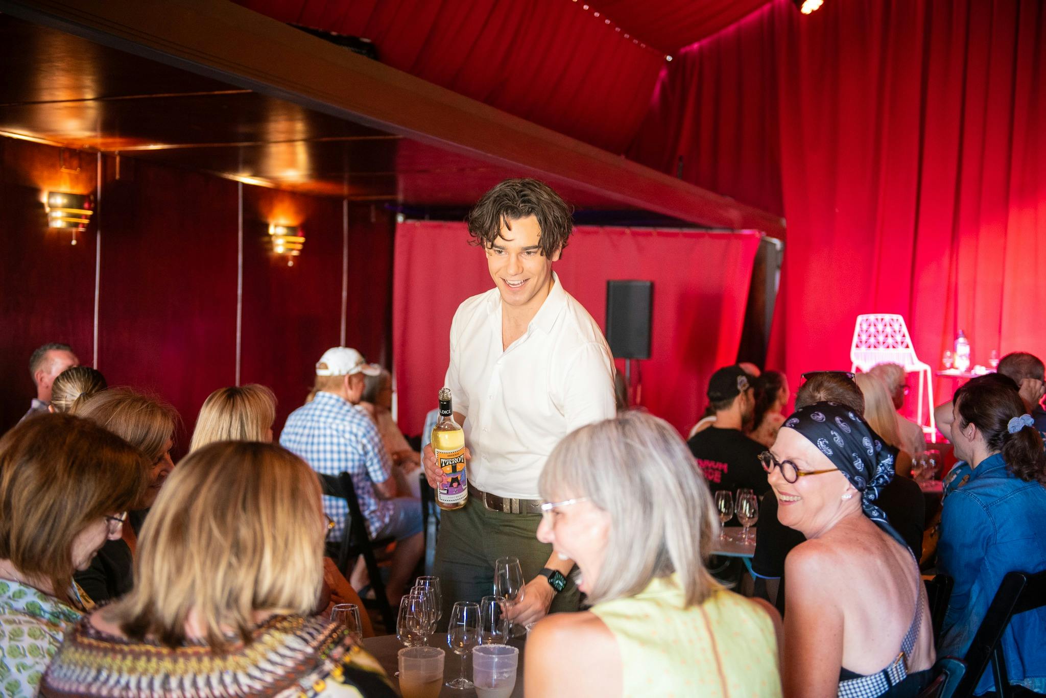 Man standing pouring wine while laughing with ladies seated at table