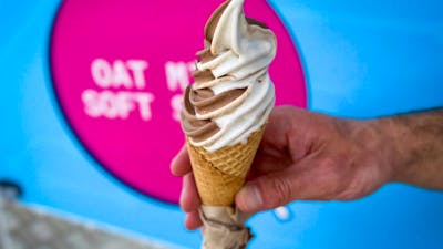 A hand holding a vanilla and chocolate soft serve icecream in a cone