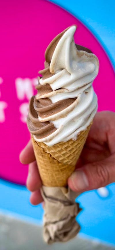 A hand holding a vanilla and chocolate soft serve icecream in a cone