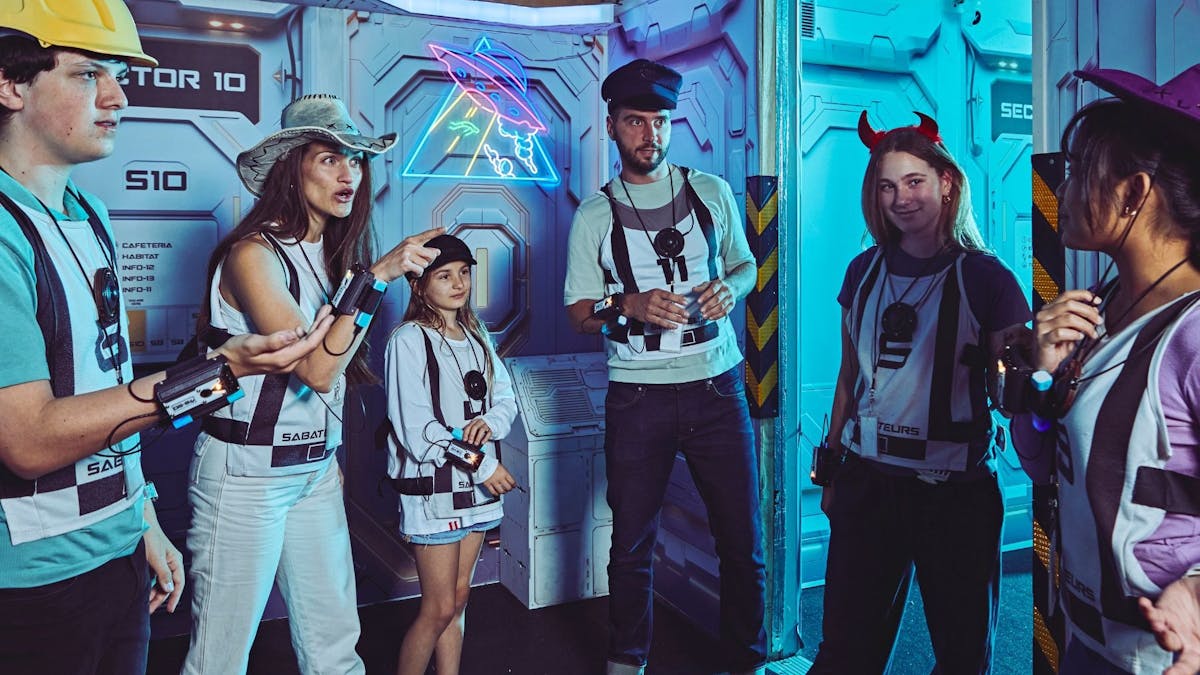 A group of adults and children in Saboteurs vests huddle mid-discussion in a corridor.