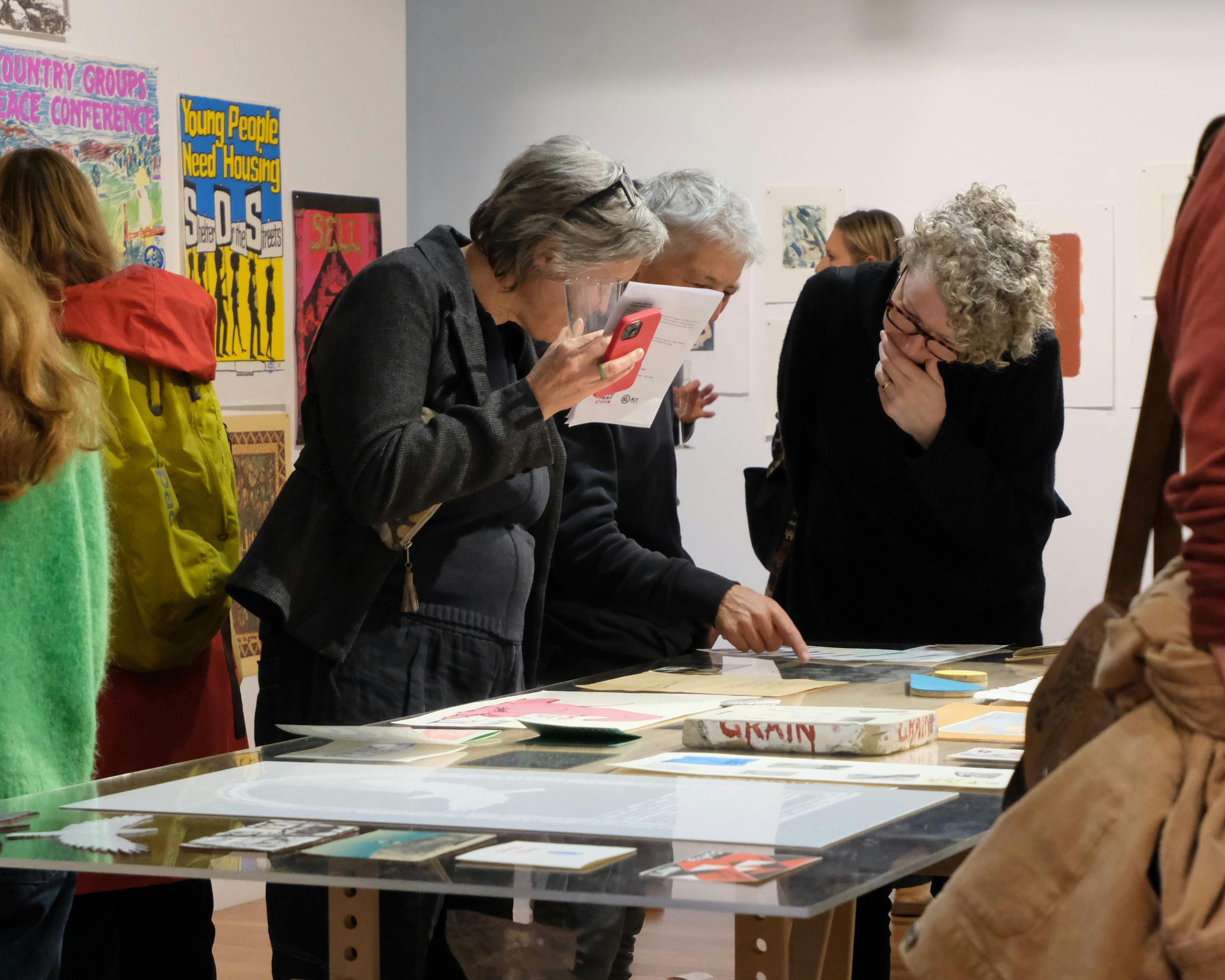 Three people look at artworks on paper upon a long table