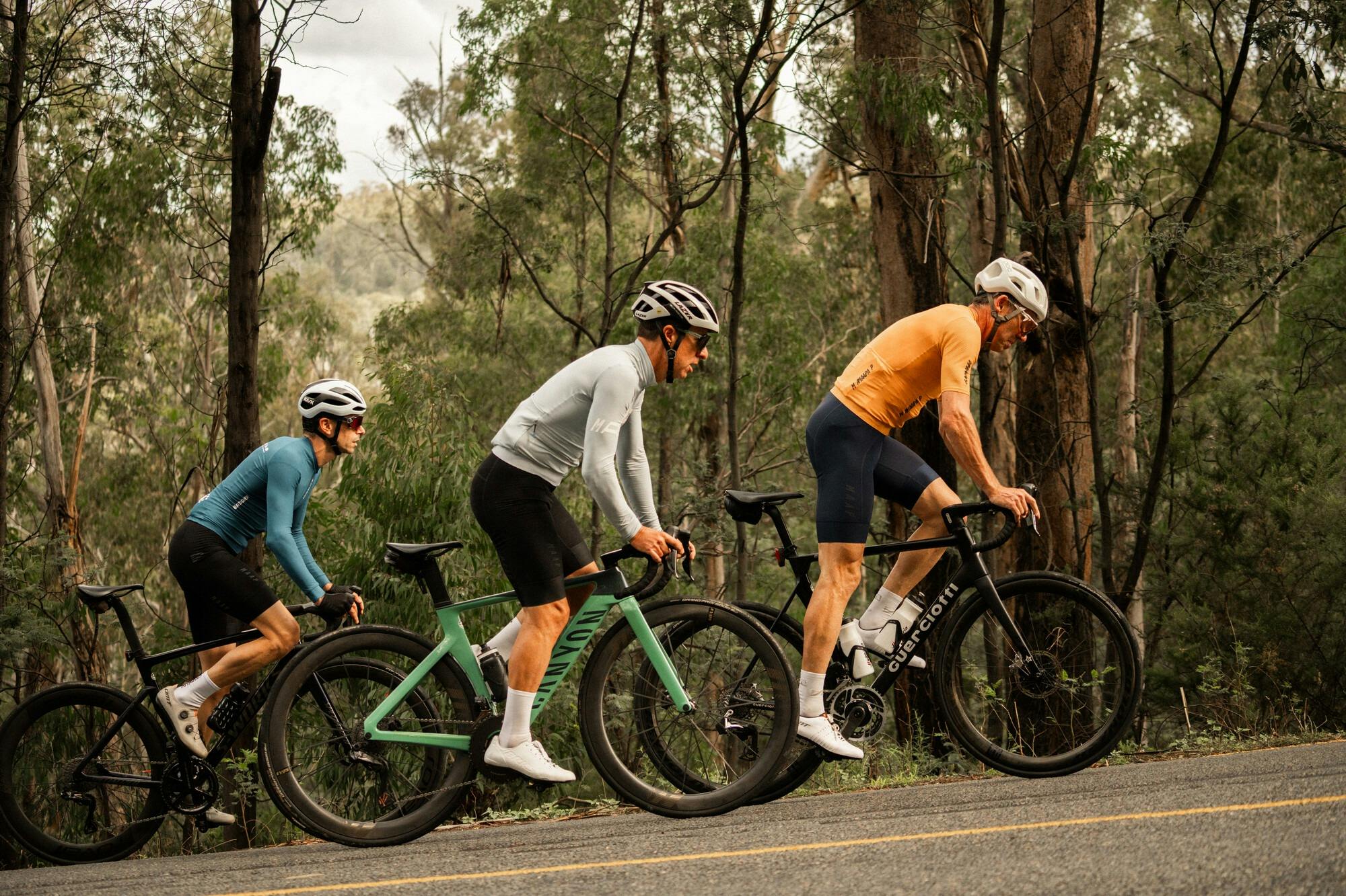 Three cyclists riding hard past native bushland on the Dinner Plain 7 Peaks Challenge route.