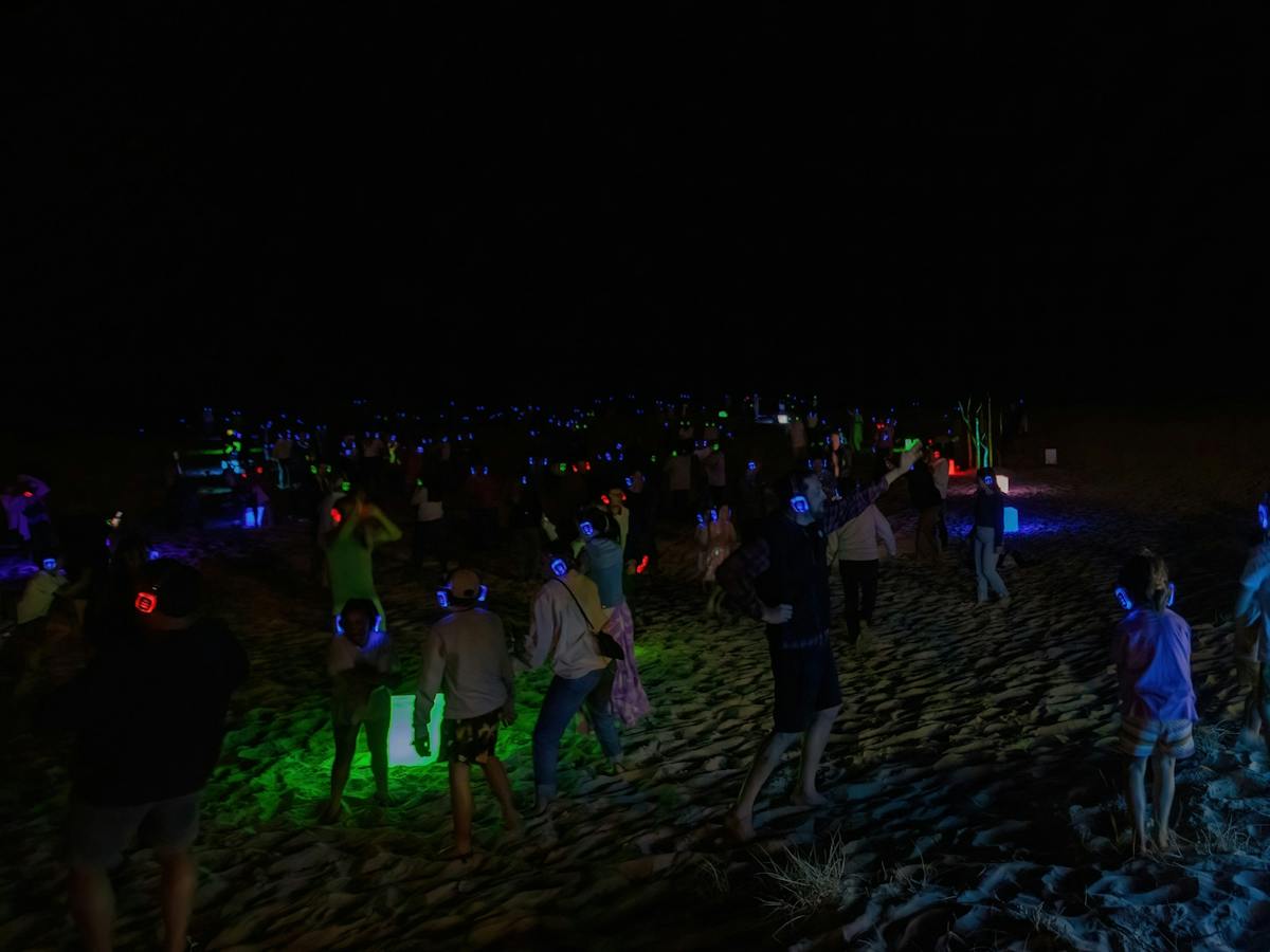 People dancing on the beach at Silent Disco Under the Stars at the 2024 SWELL Sculpture Festival