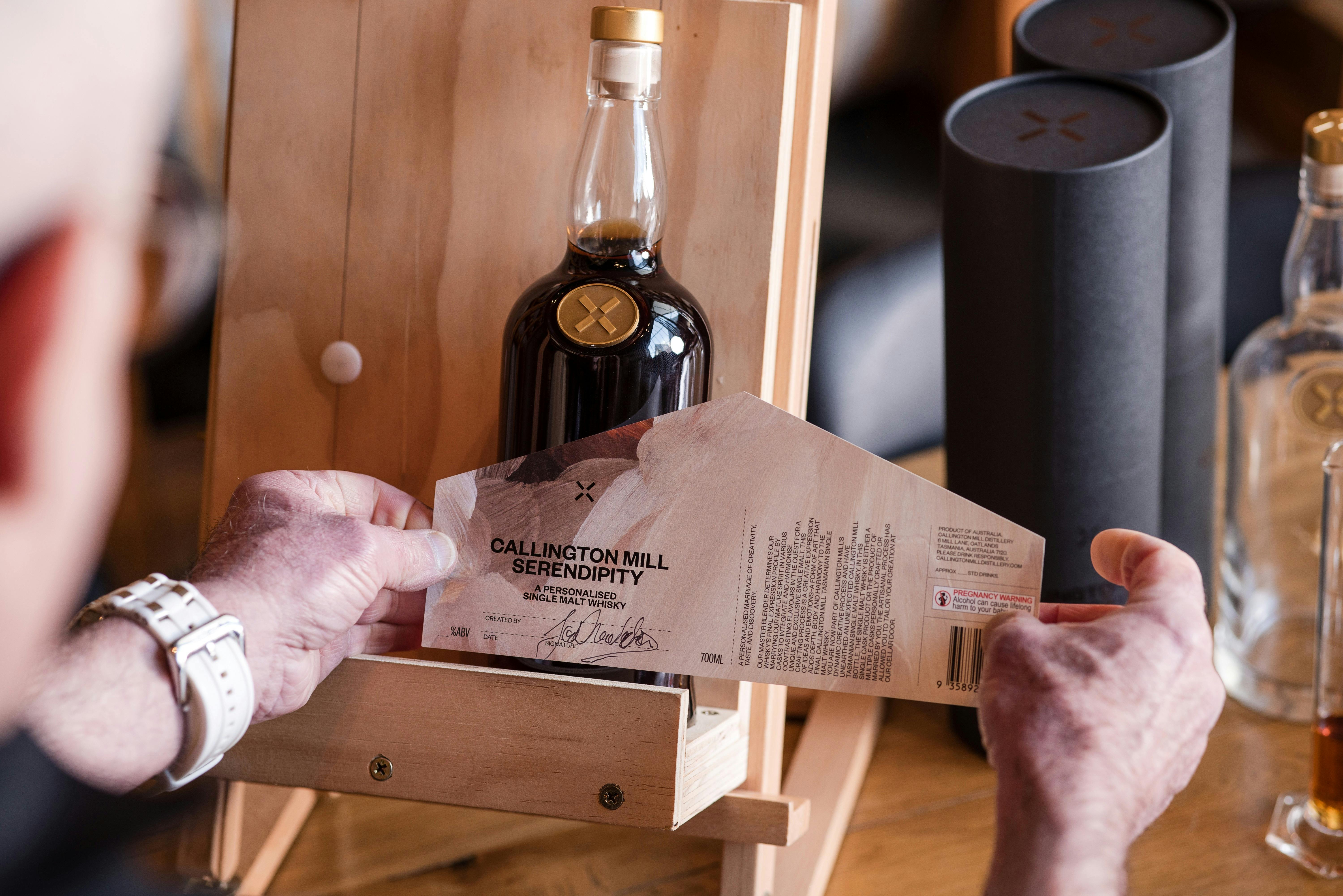 A whisky bottle on a timber easel with someone attaching a label to the bottle