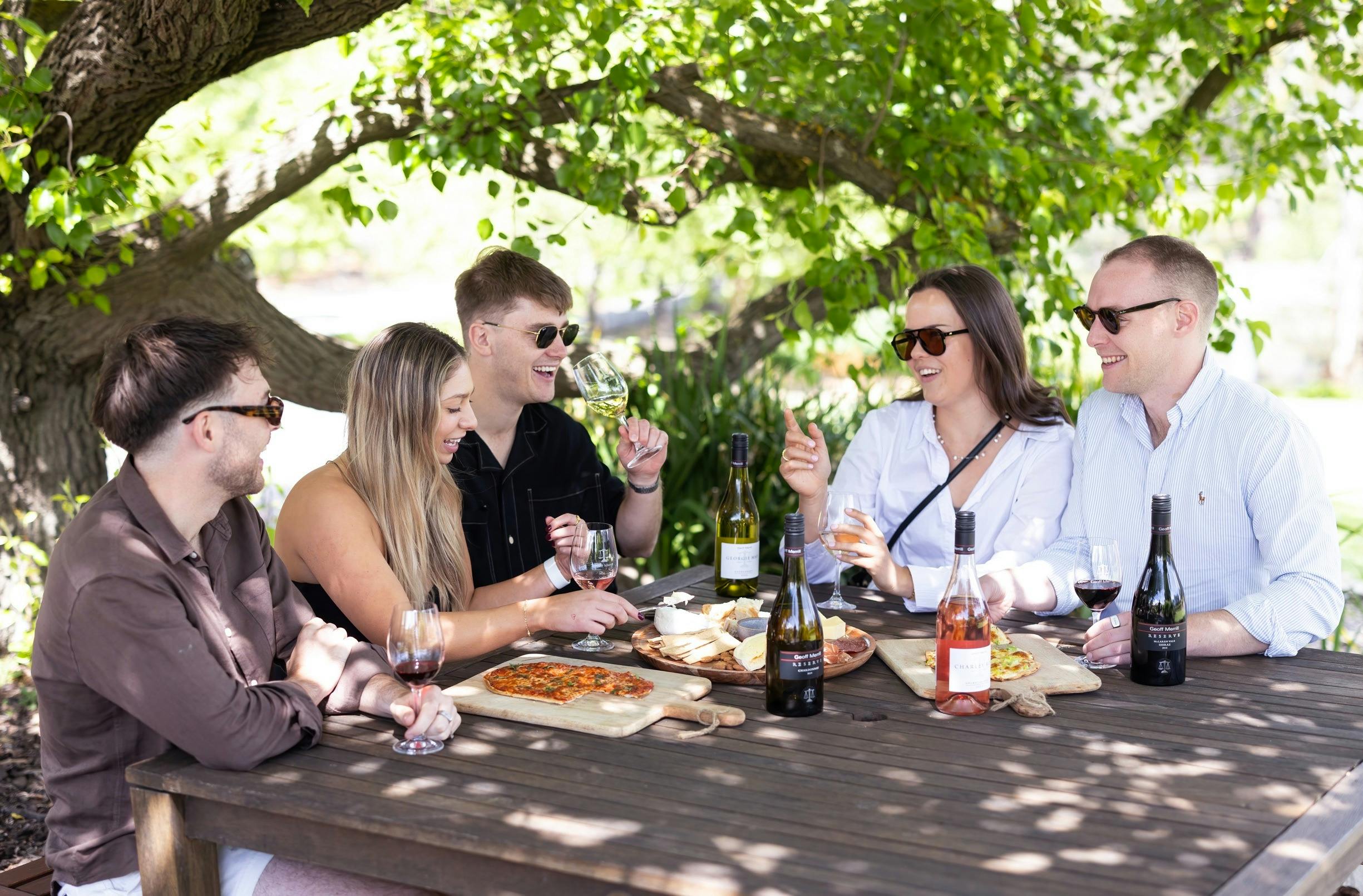 A group sitting at a table under a tree enjoying wines and cheeseboards