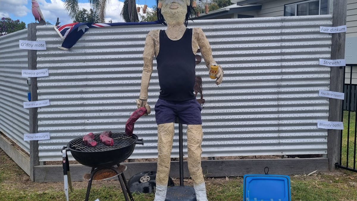 Scarecrow man cooking sausages on a barbecue.