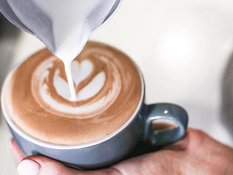 A hand pouring out milk in a cup of coffee