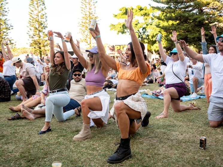 People in a yoga pose on the grass holding beers in their hands