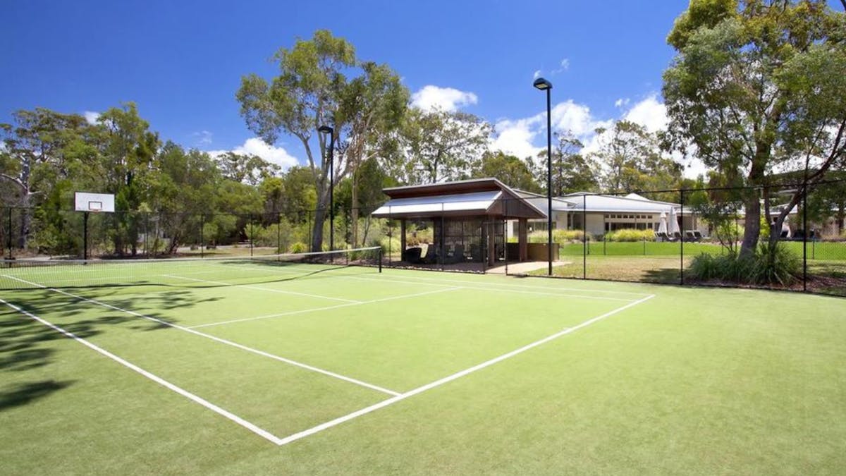Full-size tennis court and basketball court, surrounded by natural bushland.