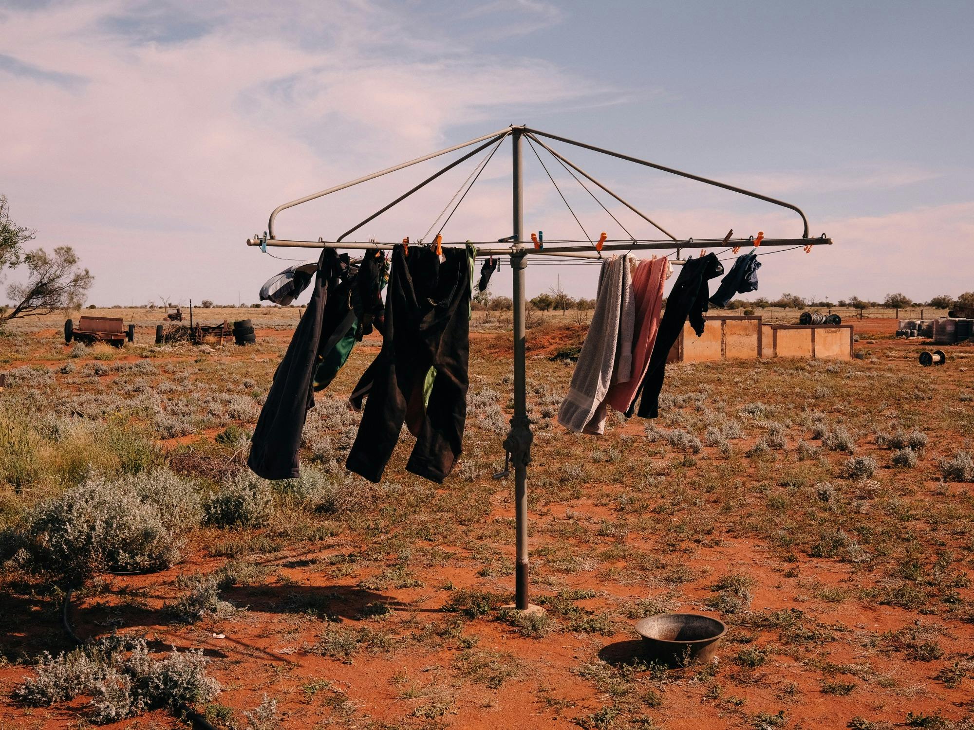 Photograph of clothes hanging on a rotary line in a dry rural landscape with red dirt and open sky