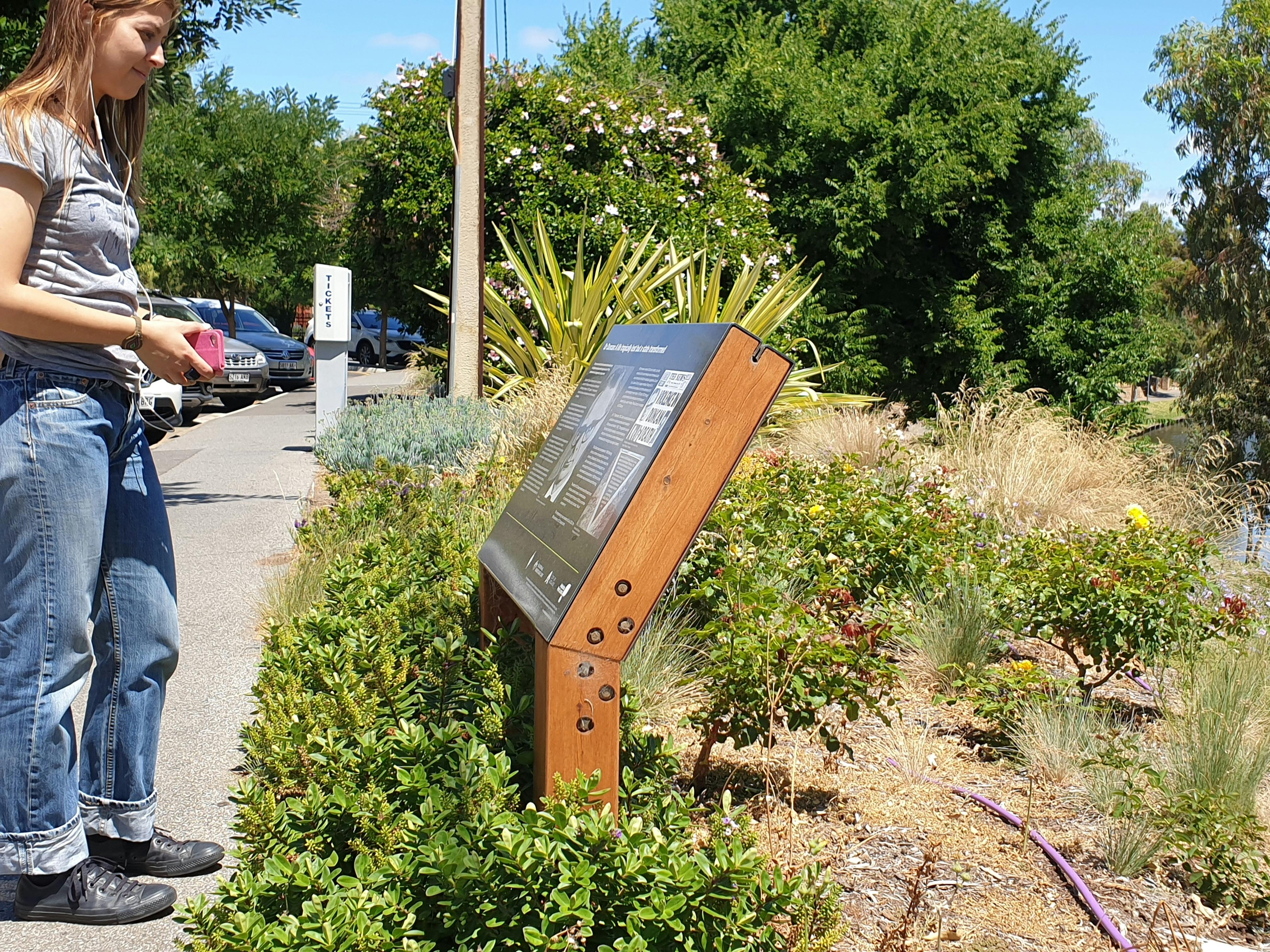 A guest listens to an audio tour while looking at a memorial infograph in Adelaide.