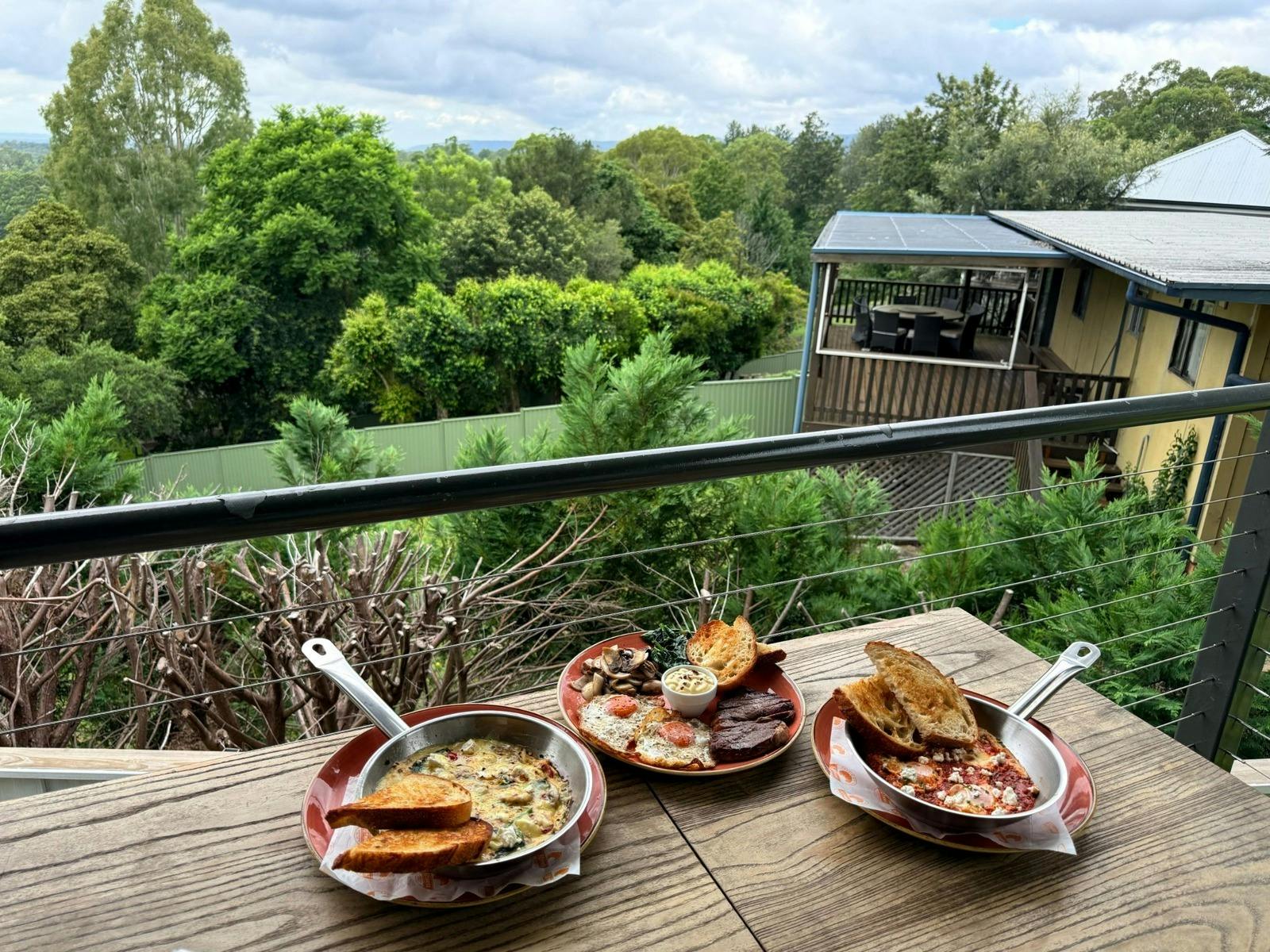 Breakfast dishes on an outdoor table overlooking the green mountain and valley scenery in Kurrajong
