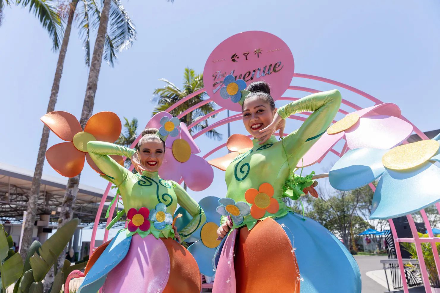 two girls dressed in flower outfits posing underneath a big pink arch arbour