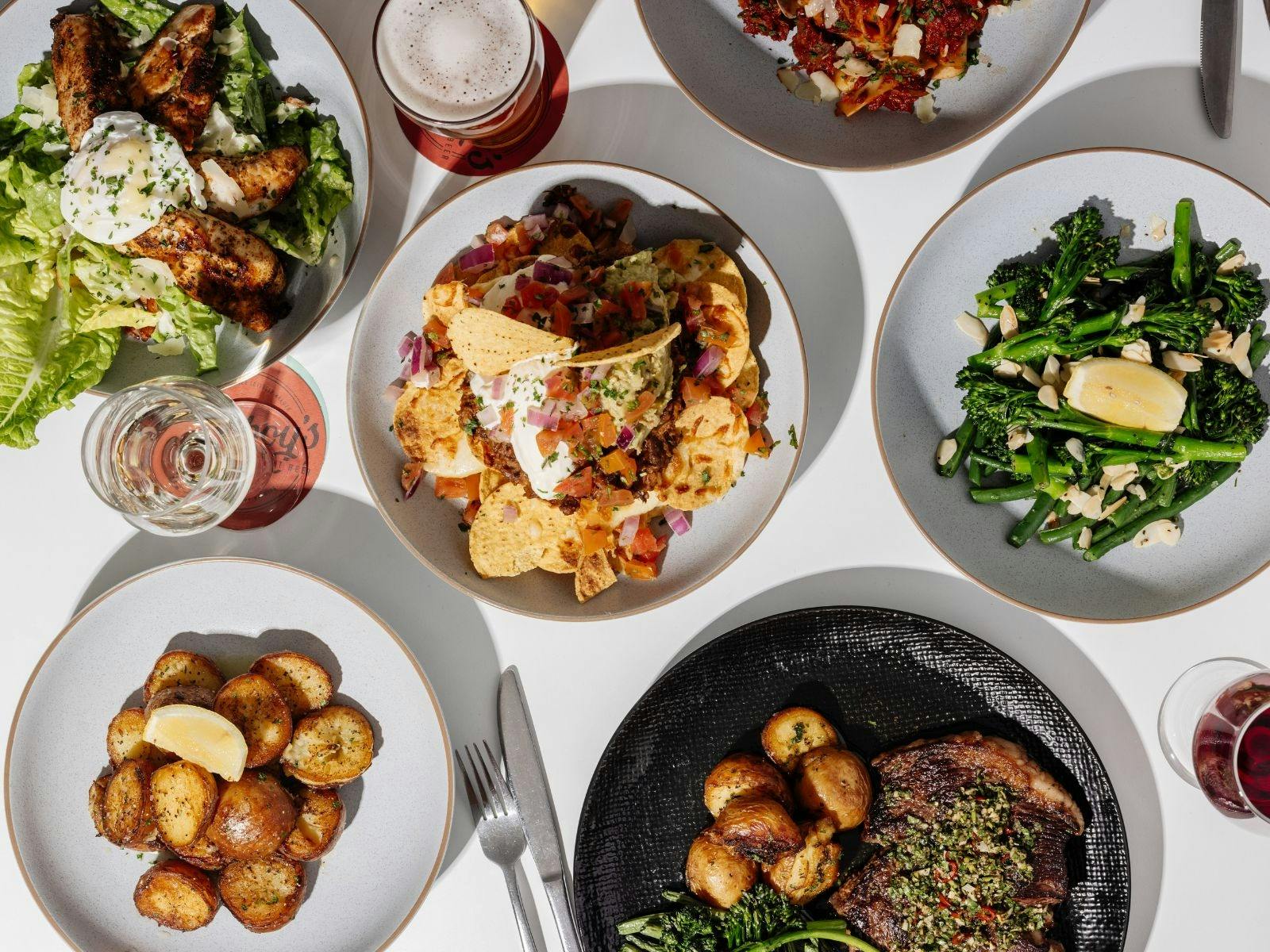 A table full of food dishes, including nachos, roast potatoes, a caesar salad and more