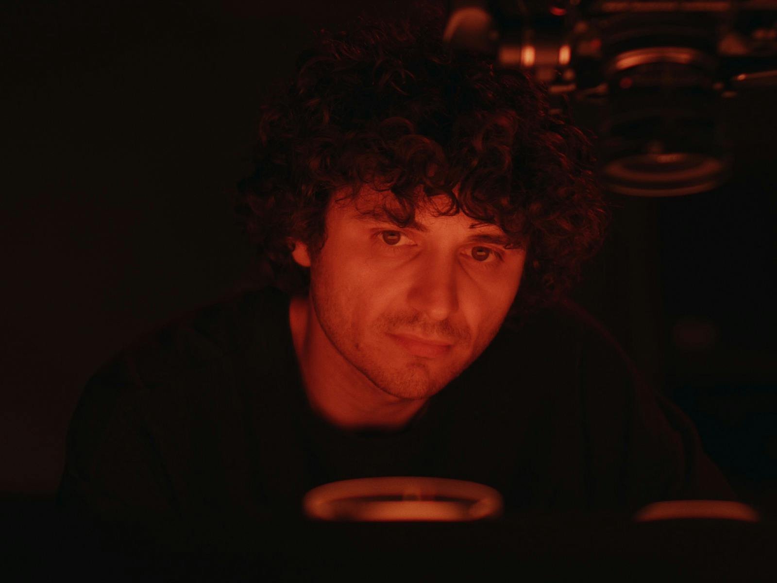 Portrait of Josef a curly-haired person illuminated by deep red light.