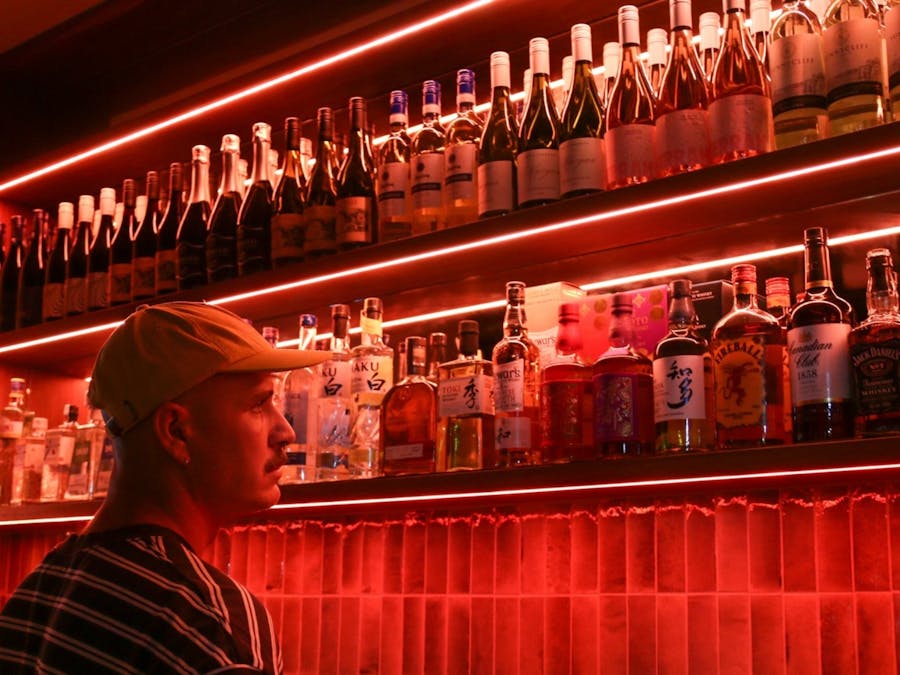 Man standing behind bar with red lighting and spirit bottles behind