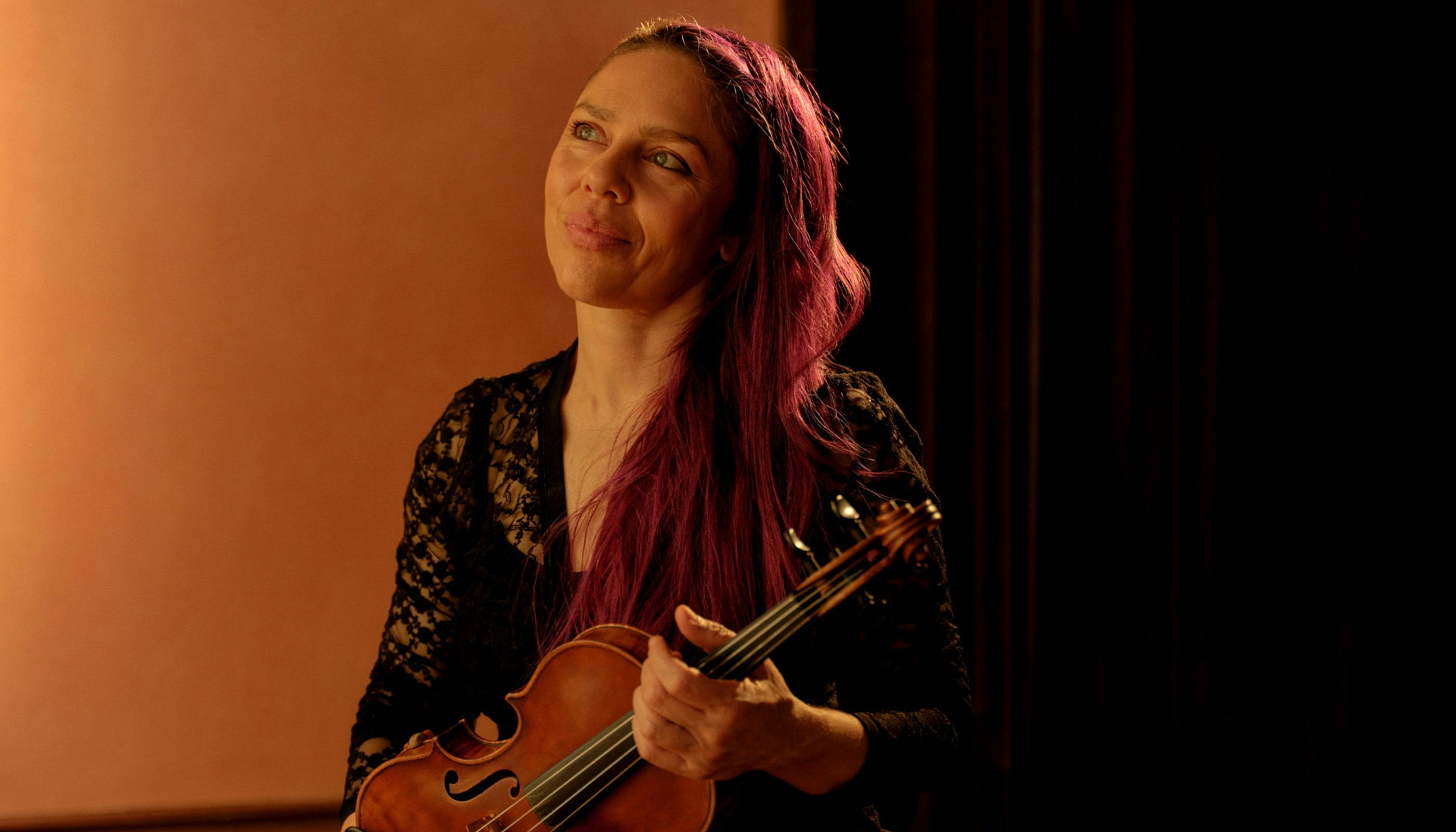 A woman holding an instrument, with an orange background.