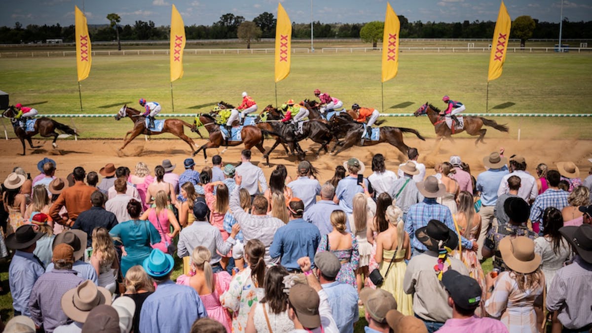 A group of people standing by a racetrack, watching horses race by