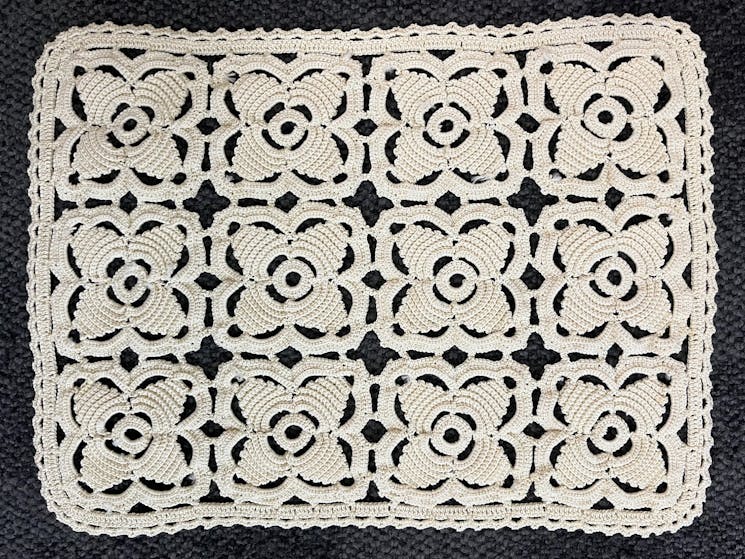 Crocheted mat with repeated pattern and cream thread