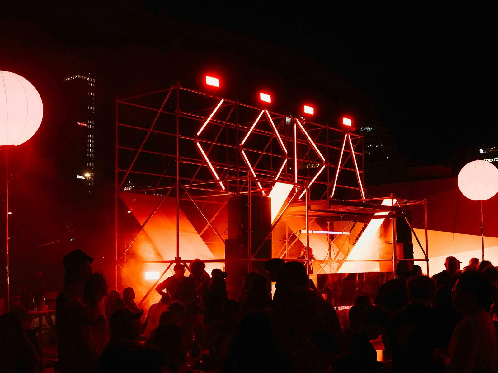 A dark image with red led lights spelling CODA on a scaffolding structure.