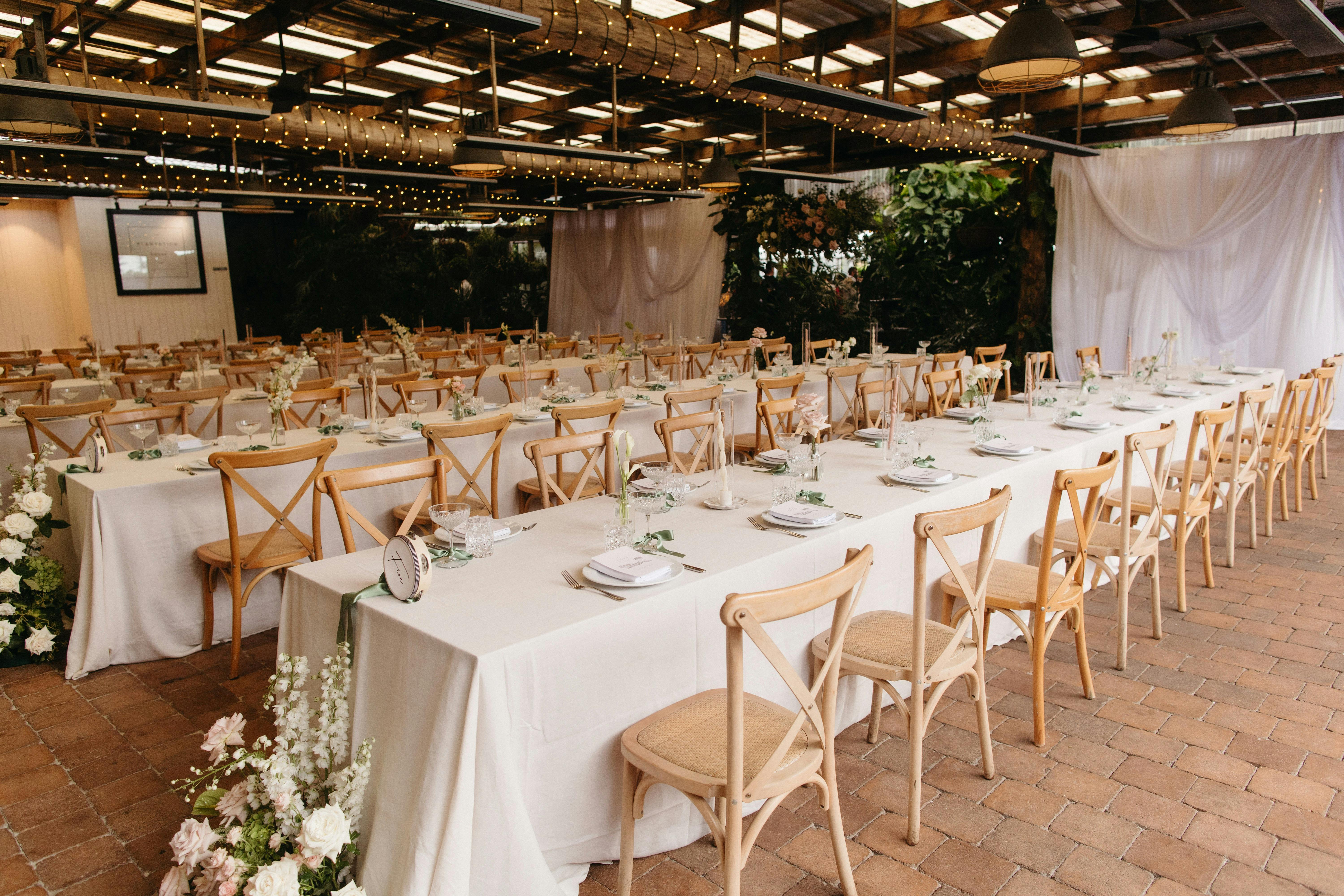 An indoor wedding reception space with tan chairs and white table cloths styled with florals