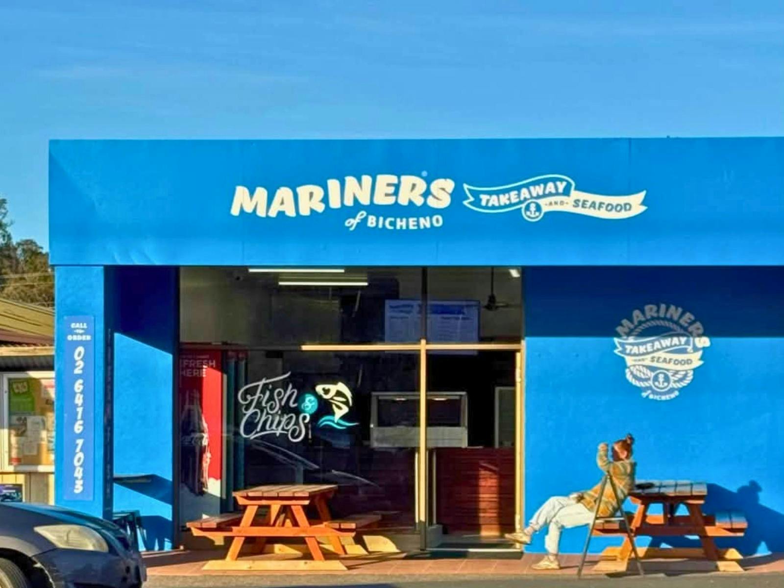 A photo of the Mariners of Bicheno shopfront in the afternoon sun with a customer sitting out front