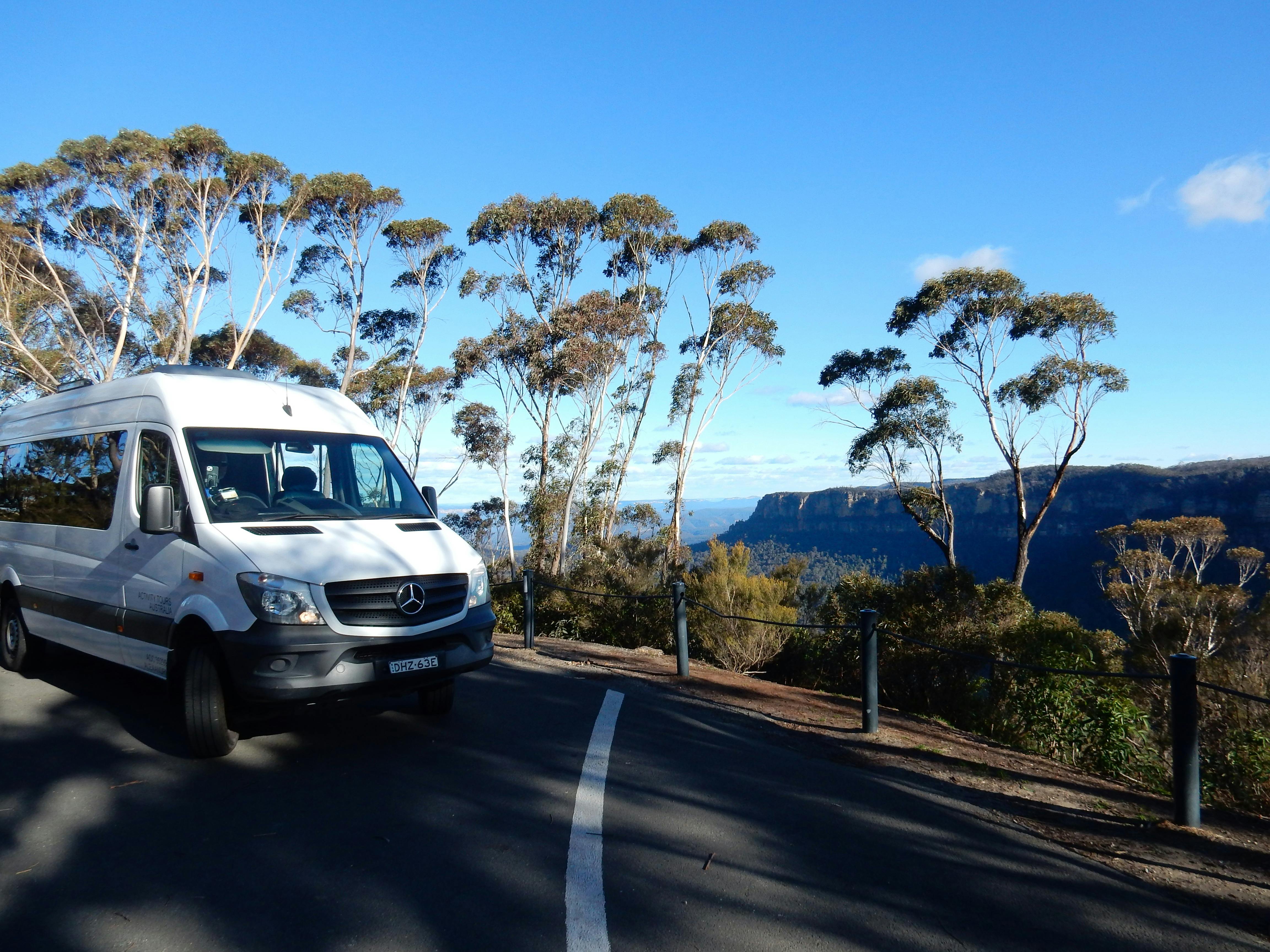 White tour bus parked at scenic Blue Mountains lookout with eucalyptus trees and valley views