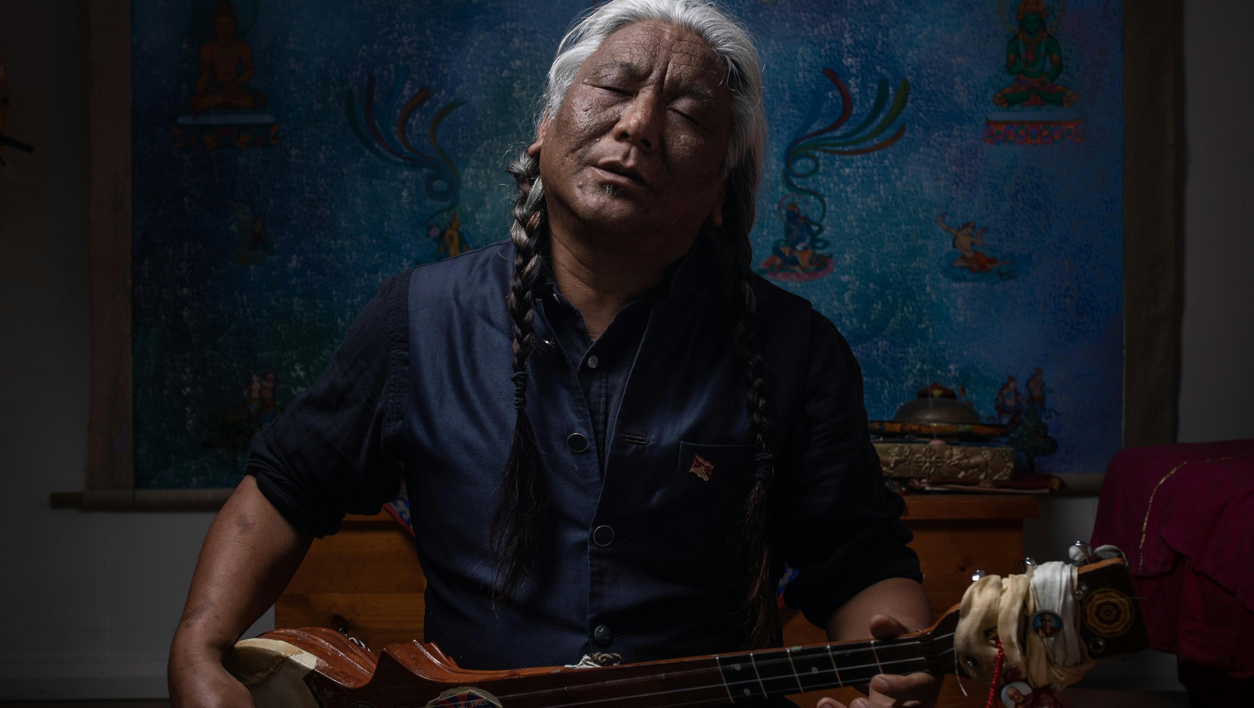 Tibetan musician Tenzin Choegyal plays a traditional stringfed instrument with his face upturned