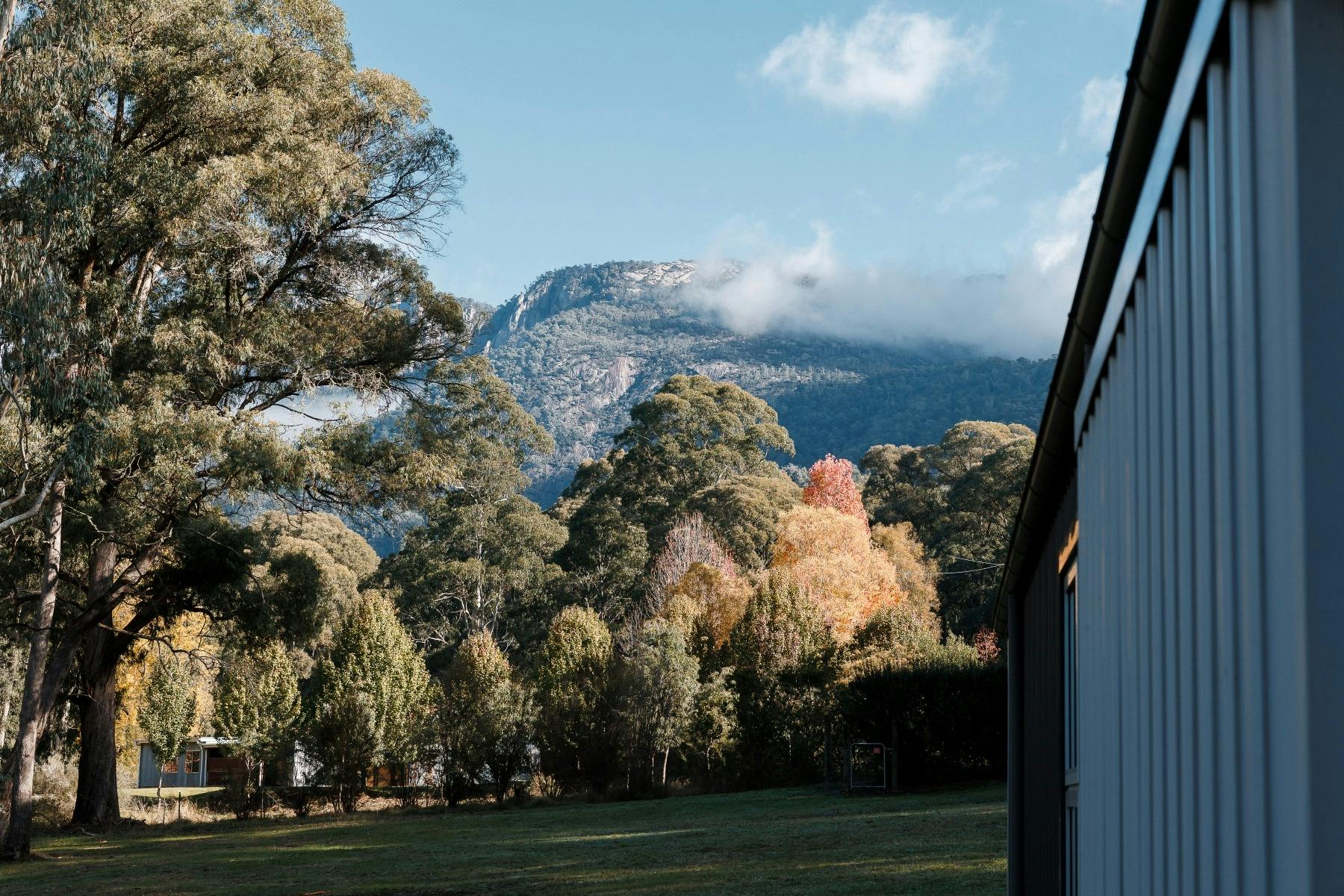 View of Mount Buffalo and side of the house, blue sky and lifting cloud above mountain